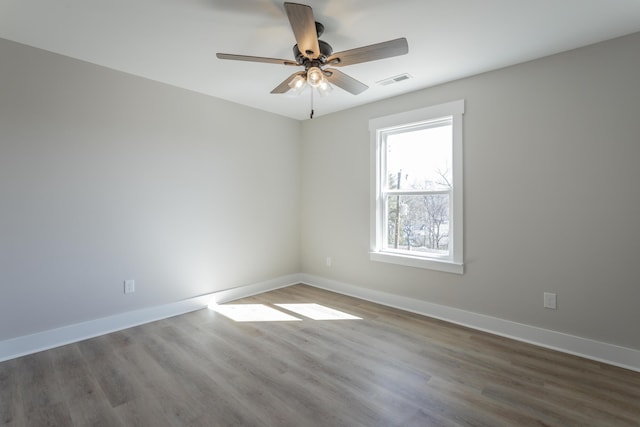 spare room with a ceiling fan, wood finished floors, visible vents, and baseboards