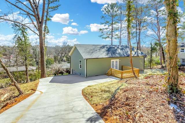 view of side of home with driveway, french doors, a shingled roof, and a wooden deck