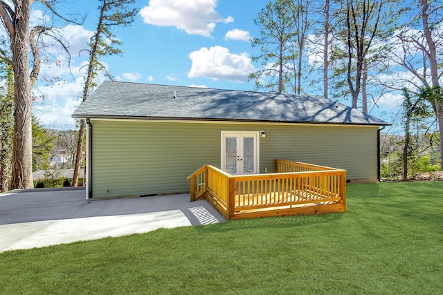 rear view of property featuring a deck, french doors, a lawn, and a shingled roof