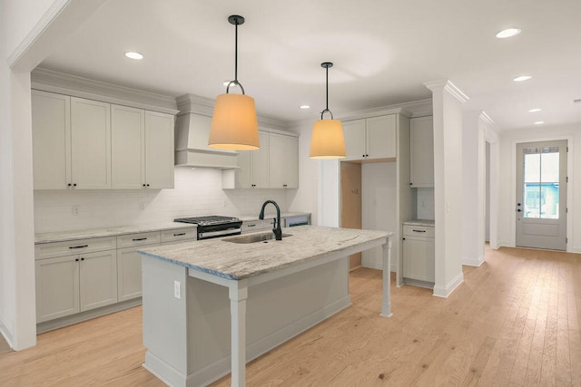 kitchen featuring a kitchen island with sink, sink, light hardwood / wood-style flooring, light stone counters, and stainless steel range with gas stovetop