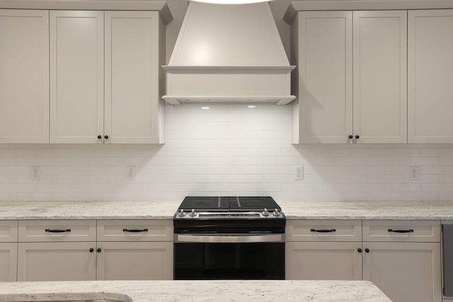 kitchen with light stone countertops, custom range hood, white cabinets, and stainless steel range oven