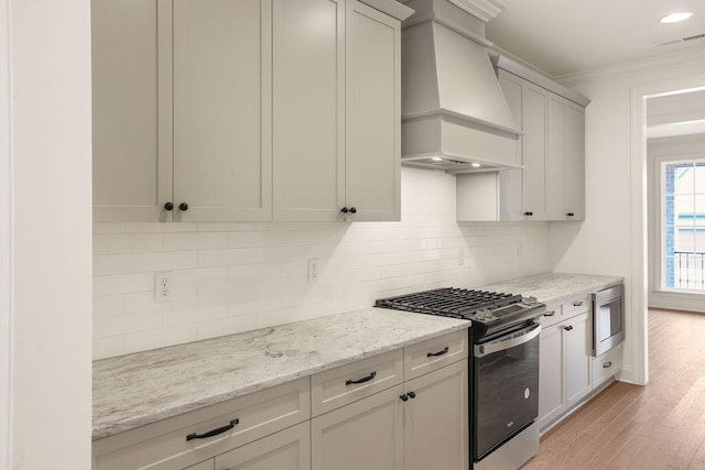 kitchen with light hardwood / wood-style flooring, custom range hood, light stone counters, white cabinetry, and stainless steel appliances