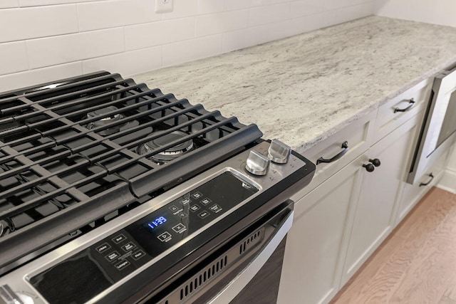 details featuring white cabinetry, stainless steel range, light stone countertops, and light hardwood / wood-style floors