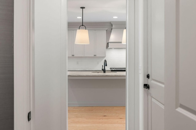 kitchen featuring light wood-type flooring, tasteful backsplash, custom range hood, sink, and pendant lighting