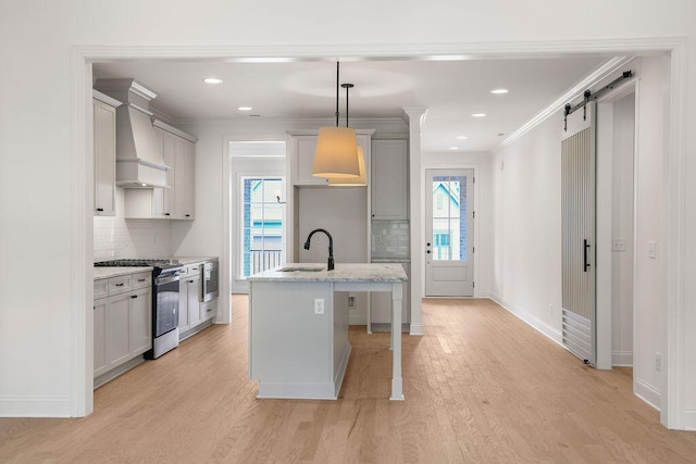 kitchen with gas stove, sink, pendant lighting, a barn door, and a center island with sink