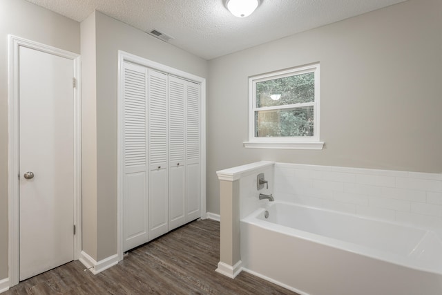 bathroom with a textured ceiling, a washtub, and hardwood / wood-style floors