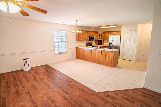 kitchen with sink, stainless steel appliances, kitchen peninsula, pendant lighting, and light hardwood / wood-style floors