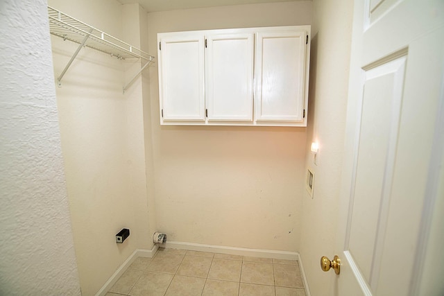 clothes washing area featuring electric dryer hookup, light tile patterned flooring, and cabinets