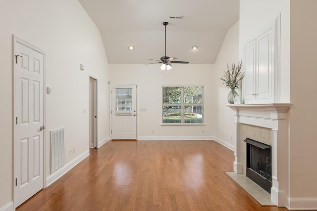 unfurnished living room with a tiled fireplace, high vaulted ceiling, light wood-type flooring, and ceiling fan