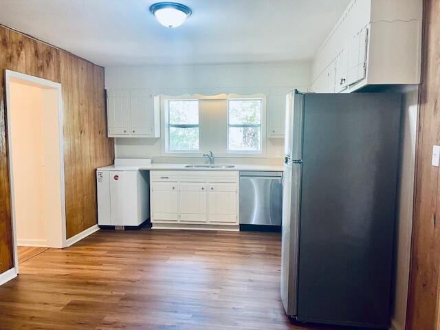 kitchen featuring stainless steel appliances, wood-type flooring, sink, white cabinetry, and wood walls