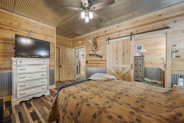 bedroom with dark hardwood / wood-style flooring, a barn door, ceiling fan, and wood walls