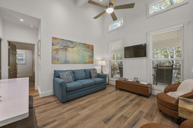 living room featuring a high ceiling, hardwood / wood-style flooring, ceiling fan, and beam ceiling