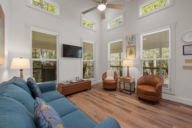 living room featuring a ceiling fan, a high ceiling, baseboards, and wood finished floors