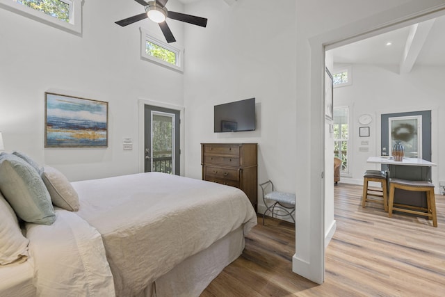 bedroom with ceiling fan, access to exterior, a towering ceiling, beamed ceiling, and wood-type flooring