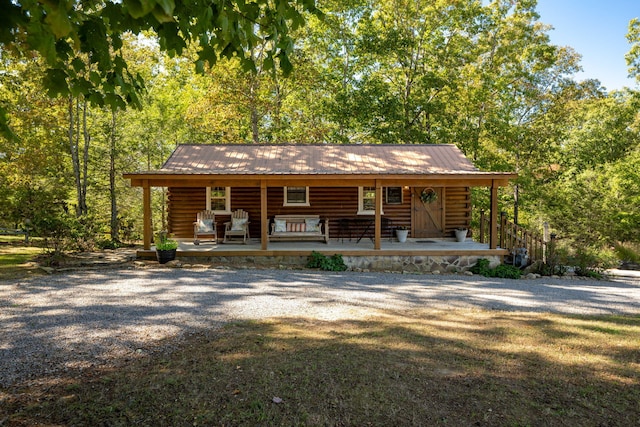 log cabin with a porch, gravel driveway, metal roof, and log exterior