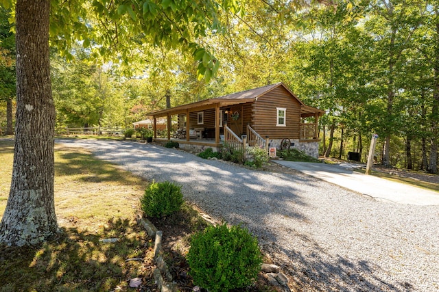 view of front of house with stone siding, a porch, gravel driveway, and log siding