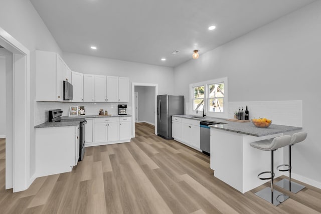 kitchen featuring a kitchen bar, appliances with stainless steel finishes, kitchen peninsula, sink, and white cabinets