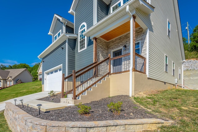 exterior space featuring an attached garage, covered porch, stone siding, and concrete driveway