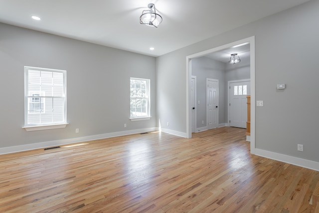 unfurnished room featuring plenty of natural light, an inviting chandelier, and light wood-type flooring