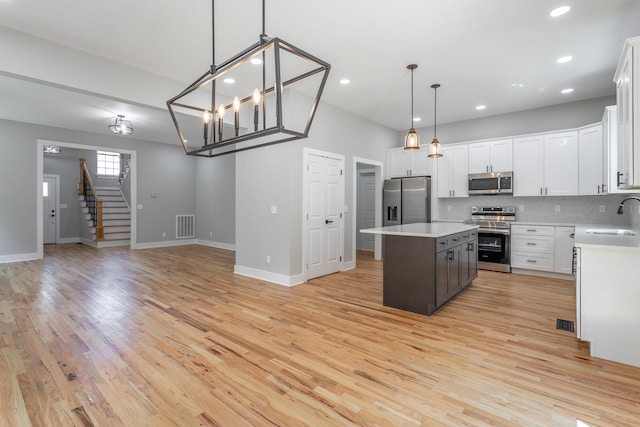 kitchen featuring a kitchen island, appliances with stainless steel finishes, a sink, light countertops, and open floor plan