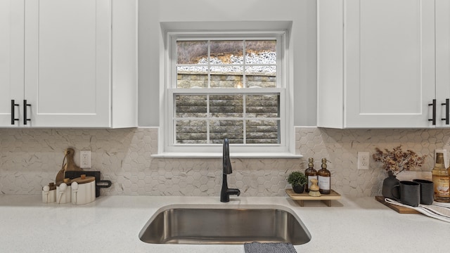 kitchen featuring backsplash, white cabinets, a sink, and light countertops