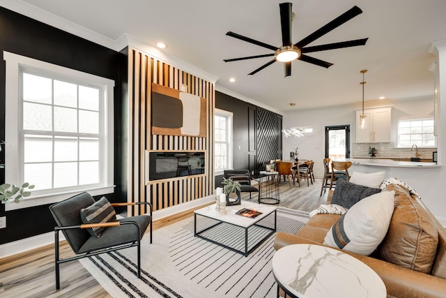 living room with light wood-type flooring, a wealth of natural light, ceiling fan, and ornamental molding