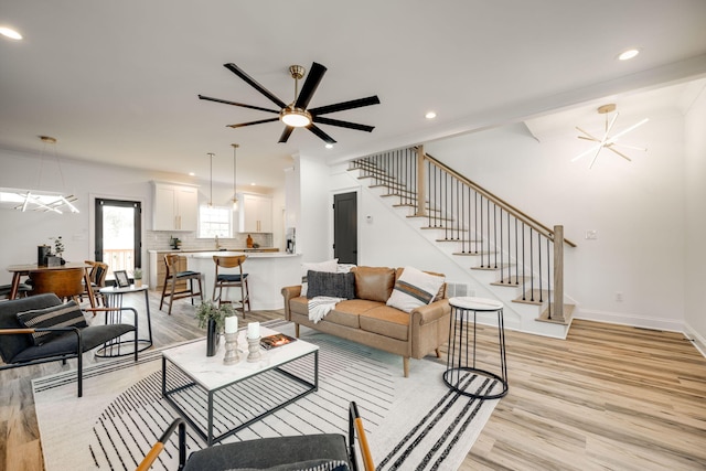 living room with sink, light hardwood / wood-style floors, and ceiling fan with notable chandelier