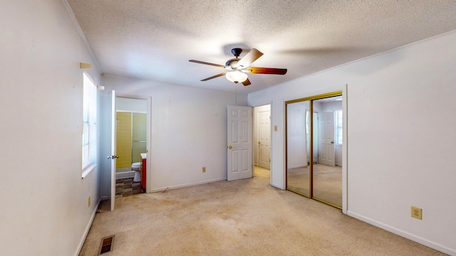 unfurnished bedroom featuring ceiling fan, a textured ceiling, ensuite bathroom, and light colored carpet