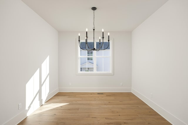 unfurnished dining area with an inviting chandelier and light wood-type flooring