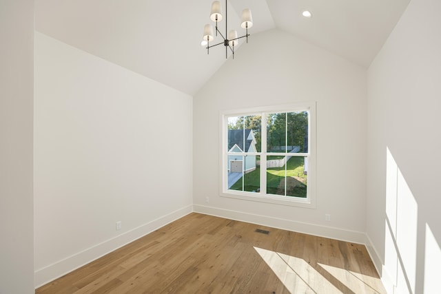 spare room featuring a notable chandelier, light wood-type flooring, and vaulted ceiling