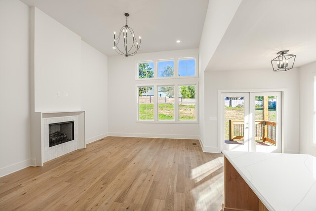 unfurnished living room with light hardwood / wood-style floors, a notable chandelier, a healthy amount of sunlight, and a tiled fireplace