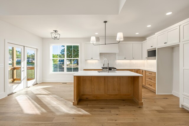 kitchen with white cabinetry, hanging light fixtures, light hardwood / wood-style floors, and an island with sink