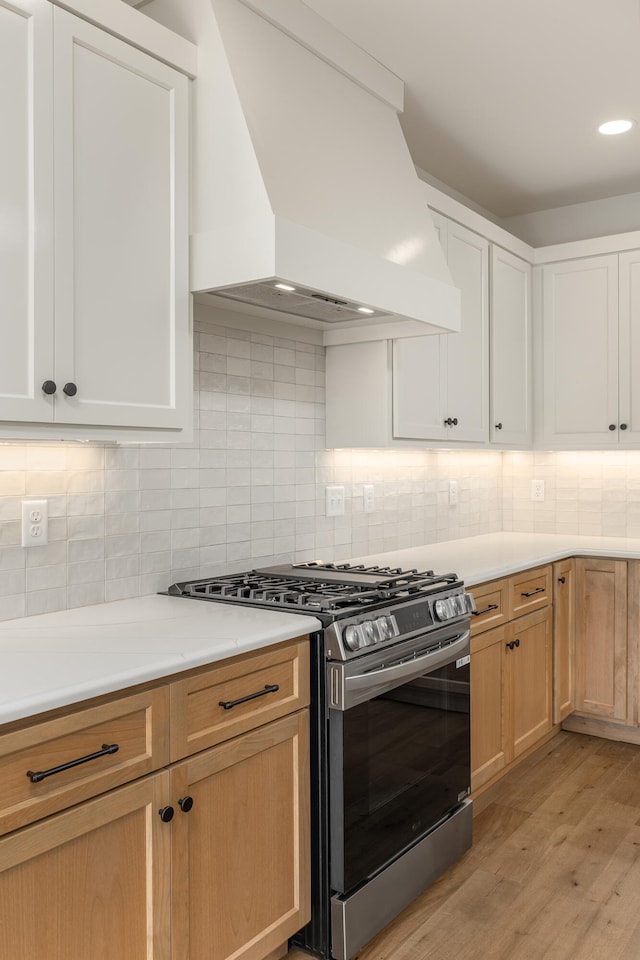 kitchen featuring stainless steel range with gas cooktop, decorative backsplash, custom range hood, and light hardwood / wood-style floors