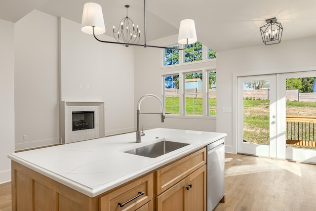 kitchen featuring a kitchen island with sink, light hardwood / wood-style flooring, hanging light fixtures, sink, and stainless steel dishwasher