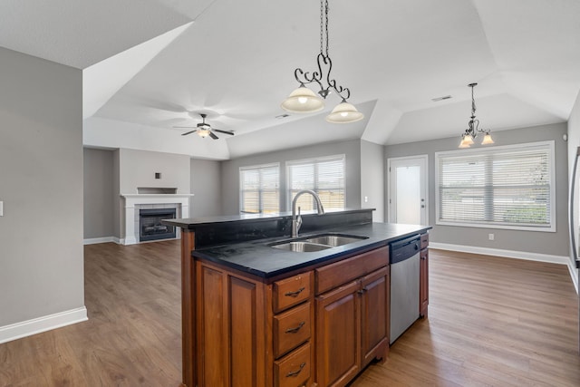 kitchen featuring wood-type flooring, sink, a kitchen island with sink, stainless steel dishwasher, and a fireplace