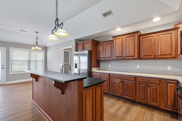 kitchen featuring light wood-type flooring, a breakfast bar, an island with sink, and stainless steel fridge