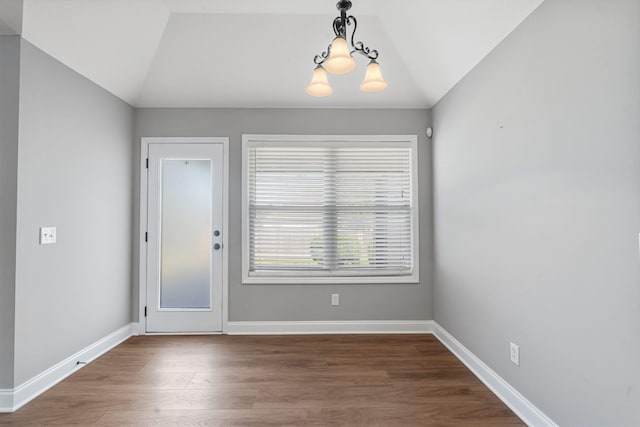 unfurnished dining area featuring hardwood / wood-style floors, a notable chandelier, and vaulted ceiling