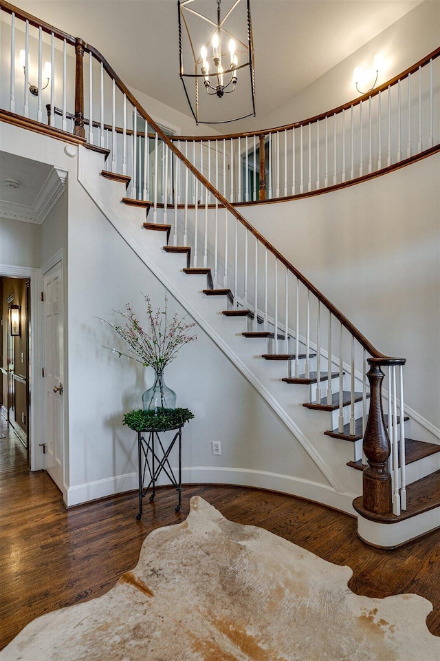 staircase featuring crown molding, wood-type flooring, a high ceiling, and a notable chandelier