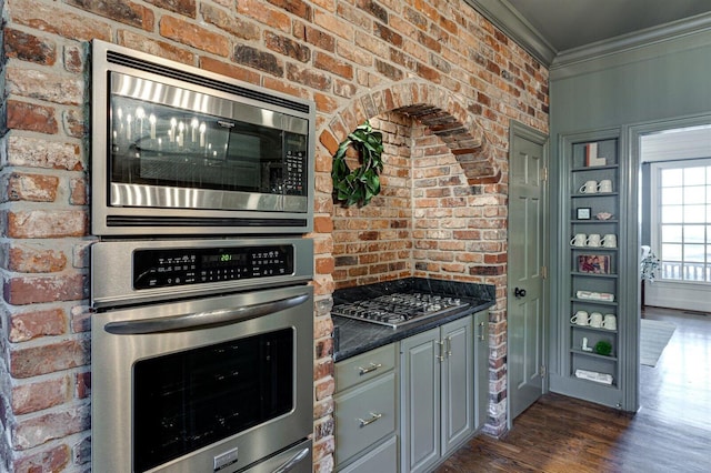 kitchen featuring brick wall, gray cabinetry, ornamental molding, stainless steel appliances, and dark wood-type flooring