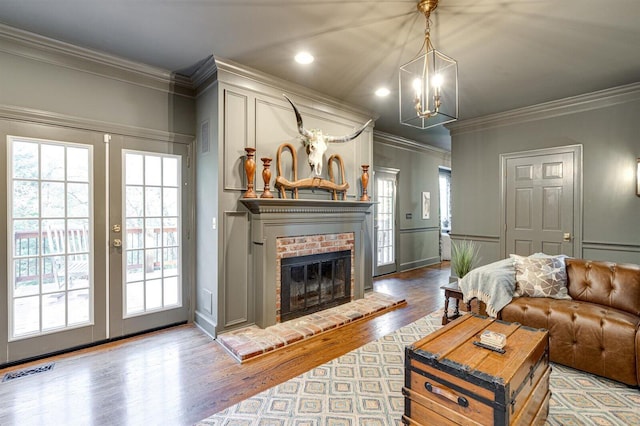 living room with french doors, wood-type flooring, crown molding, and a brick fireplace