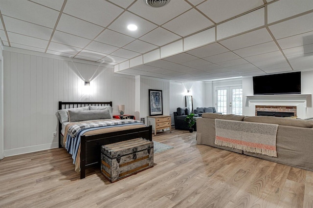 bedroom featuring a drop ceiling, a brick fireplace, wood-type flooring, and french doors