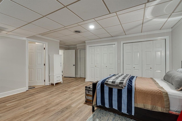 bedroom featuring multiple closets, crown molding, a paneled ceiling, and hardwood / wood-style floors