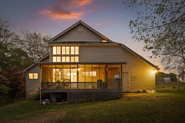 back house at dusk with covered porch and a lawn