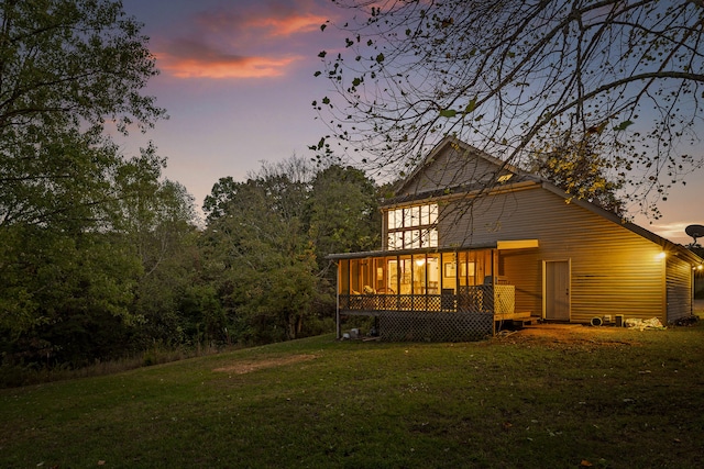 back house at dusk featuring a sunroom and a lawn