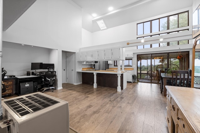 kitchen with white cabinetry, light wood-type flooring, high vaulted ceiling, and stainless steel refrigerator