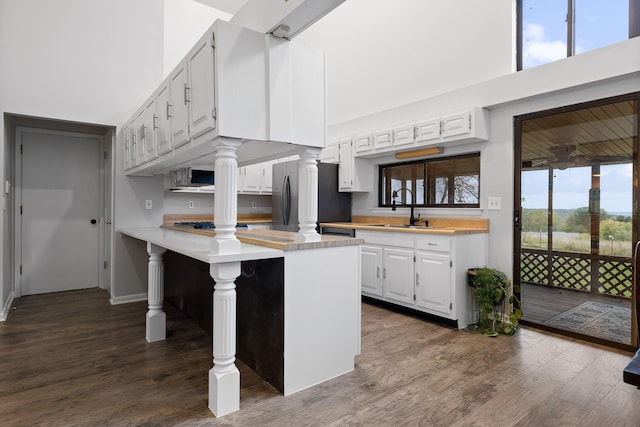 kitchen featuring dark wood-type flooring, white cabinets, kitchen peninsula, and stainless steel refrigerator