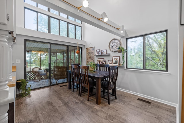 dining space featuring a towering ceiling, hardwood / wood-style flooring, and decorative columns