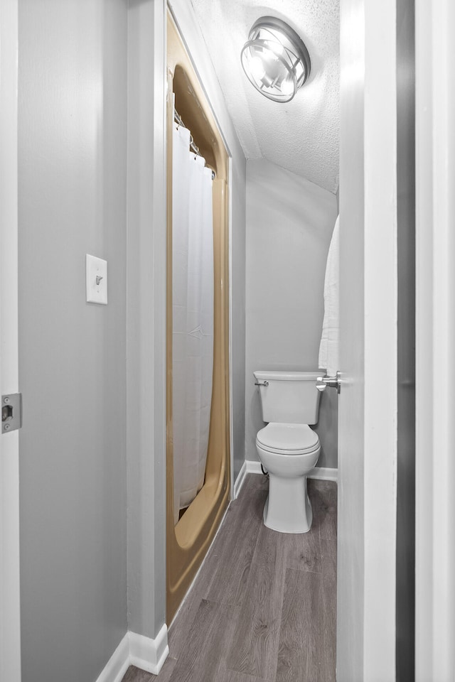 bathroom featuring toilet, hardwood / wood-style floors, a shower with curtain, and a textured ceiling