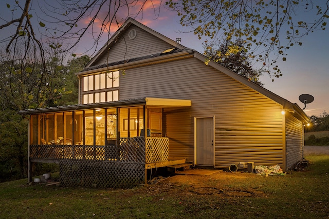 back house at dusk featuring a sunroom and a lawn