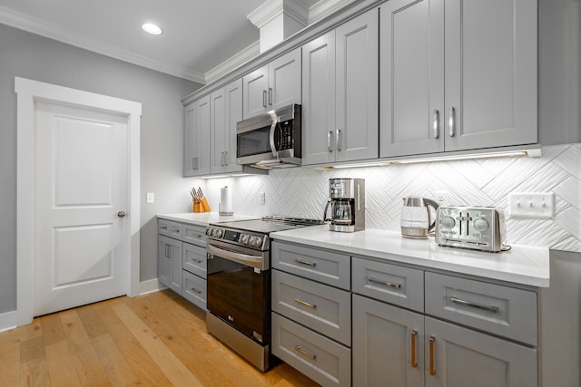 kitchen featuring decorative backsplash, stainless steel appliances, crown molding, light wood-type flooring, and gray cabinets